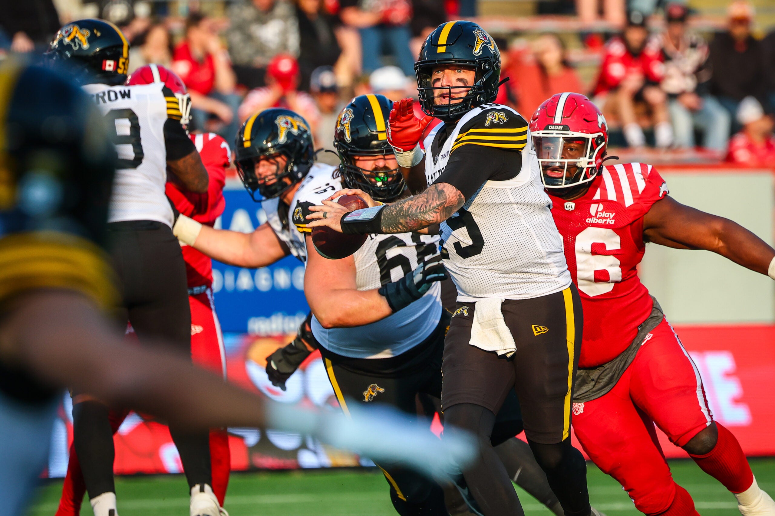 Jun 7, 2025; Calgary, Alberta, Canada; Hamilton Tiger-Cats quarterback Bo Levi Mitchell (19) looks to pass against the Calgary Stampeders with Jaylon Hutchings (96) chasing him down during the second half at McMahon Stadium.