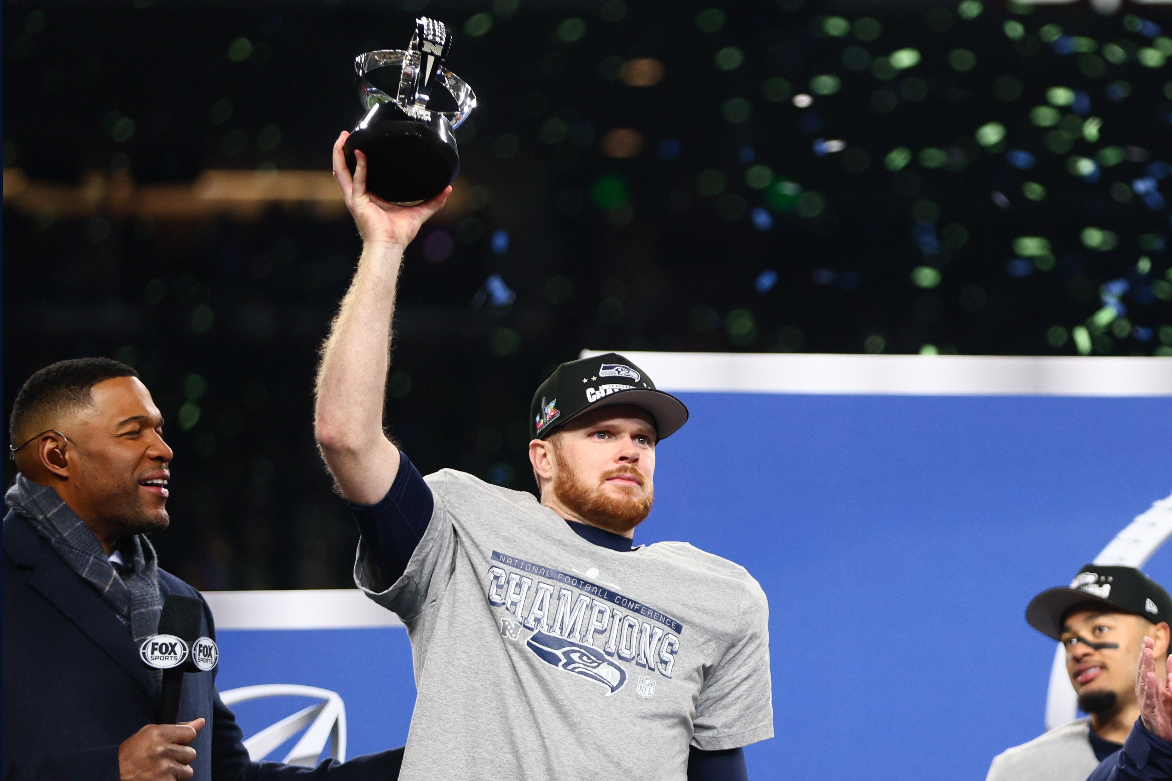 Jan 25, 2026; Seattle, WA, USA; Seattle Seahawks quarterback Sam Darnold (14) celebrates with the trophy on the podium after defeating the Los Angeles Rams in the 2026 NFC Championship Game at Lumen Field.