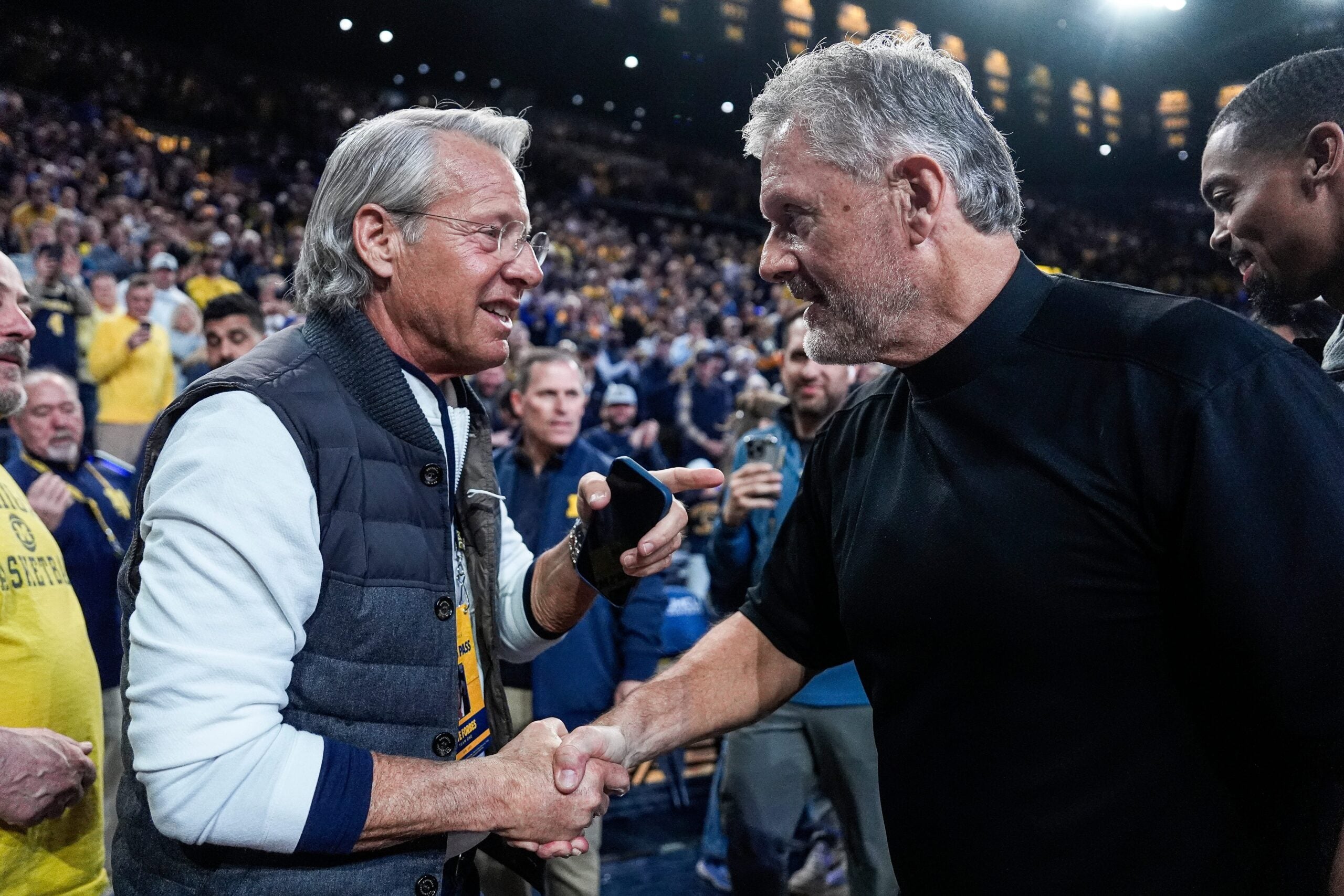 Nate Forbes, left, talks to football head coach Kyle Whittingham after him being introduced on the court during the first half between Michigan and USC at Crisler Center in Ann Arbor on Friday, Jan. 2, 2026.