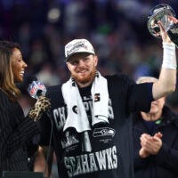 Feb 8, 2026; Santa Clara, CA, USA; Seattle Seahawks quarterback Sam Darnold (14) celebrates with the Vince Lombardi trophy on the podium after defeating the New England Patriots in Super Bowl LX at Levi's Stadium.