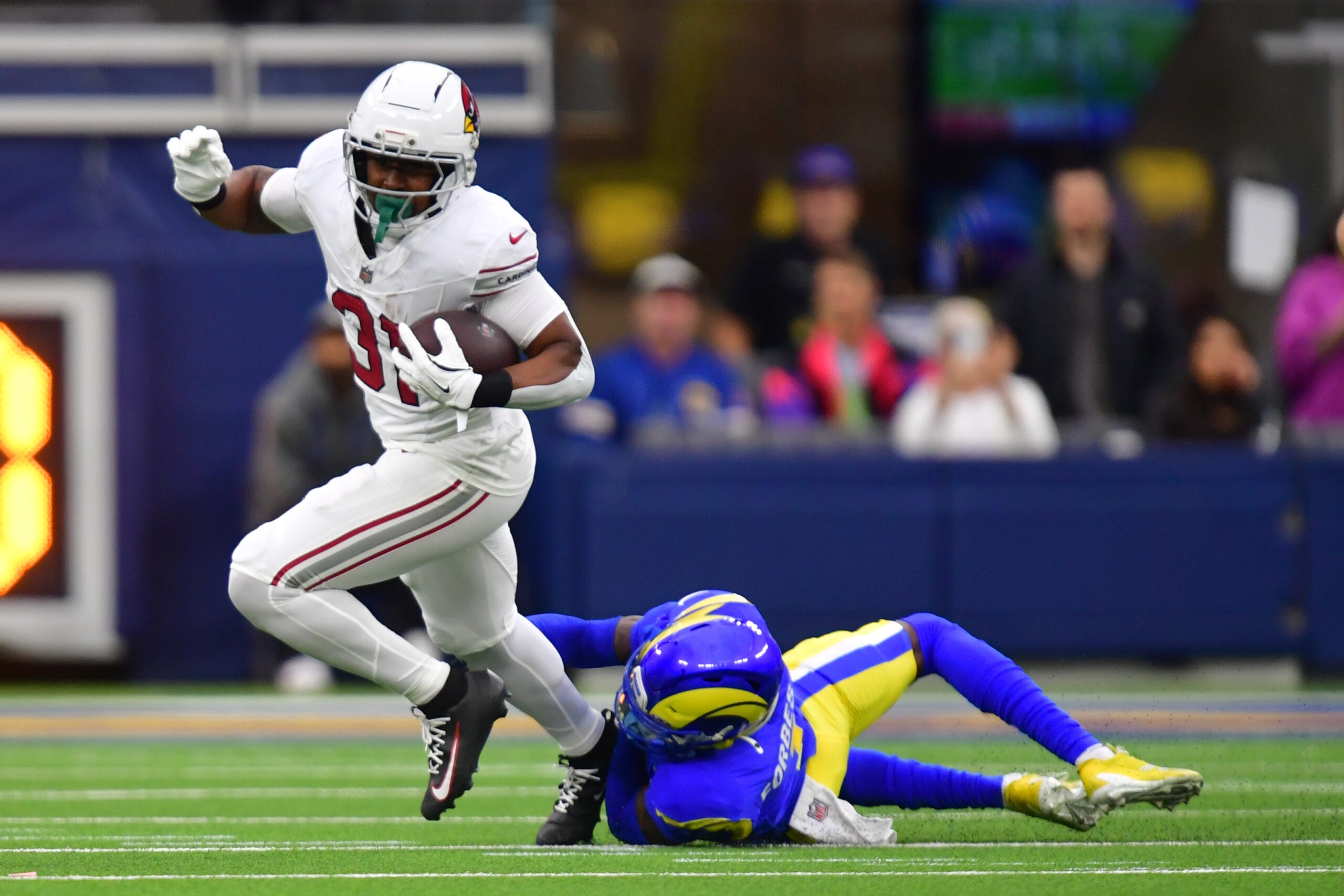 Jan 4, 2026; Inglewood, California, USA; Arizona Cardinals running back Emari Demercado (31) carries the ball as Los Angeles Rams cornerback Emmanuel Forbes Jr. (1) defends during the second half at SoFi Stadium.
