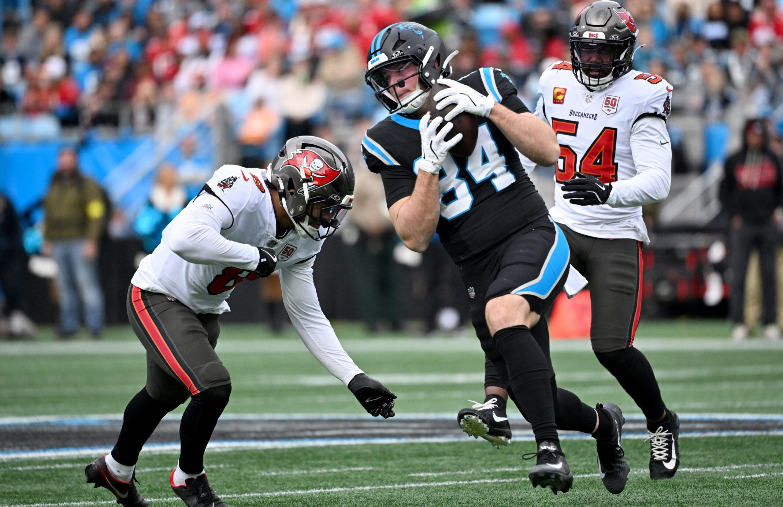 Dec 21, 2025; Charlotte, North Carolina, USA; Carolina Panthers tight end Mitchell Evans (84) runs against Tampa Bay Buccaneers linebacker Sirvocea Dennis (8) and linebacker Lavonte David (54) during the first half at Bank of America Stadium.