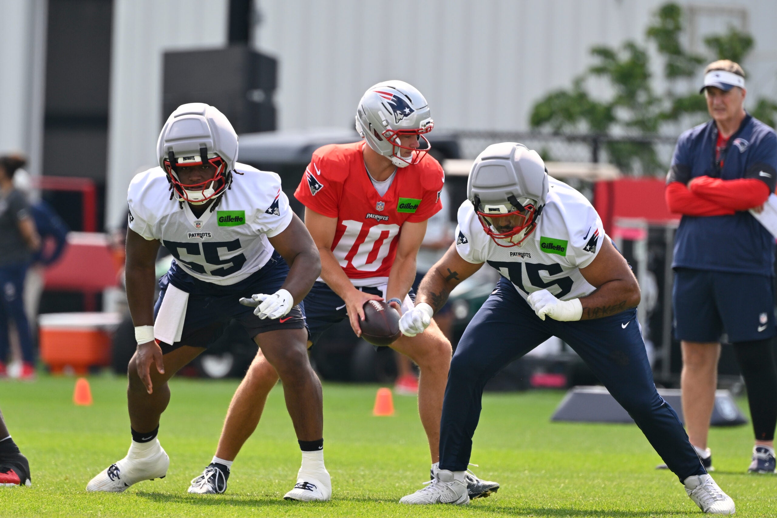 Jul 28, 2026; Foxborough, MA, USA; New England Patriots offensive lineman Jared Wilson (55) and guard Alijah Vera-Tucker (75) do a drill with quarterback Drake Maye (10) during training camp at Gillette Stadium.