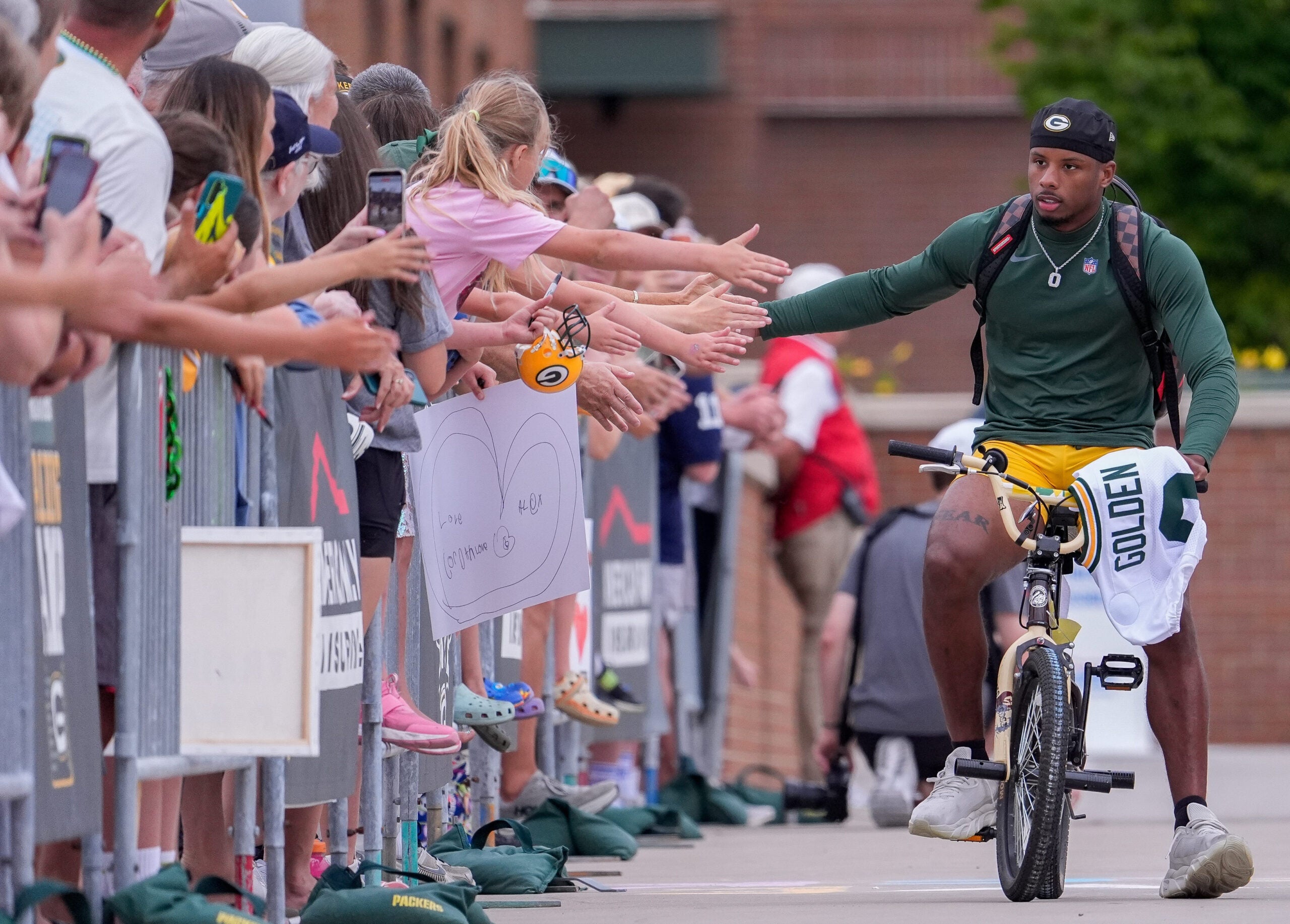 Green Bay Packers wide receiver Matthew Golden slaps hands with fans as he rides a bicycle to practice on Friday, July 31, 2026, at Lambeau Field in Green Bay, Wisconsin.