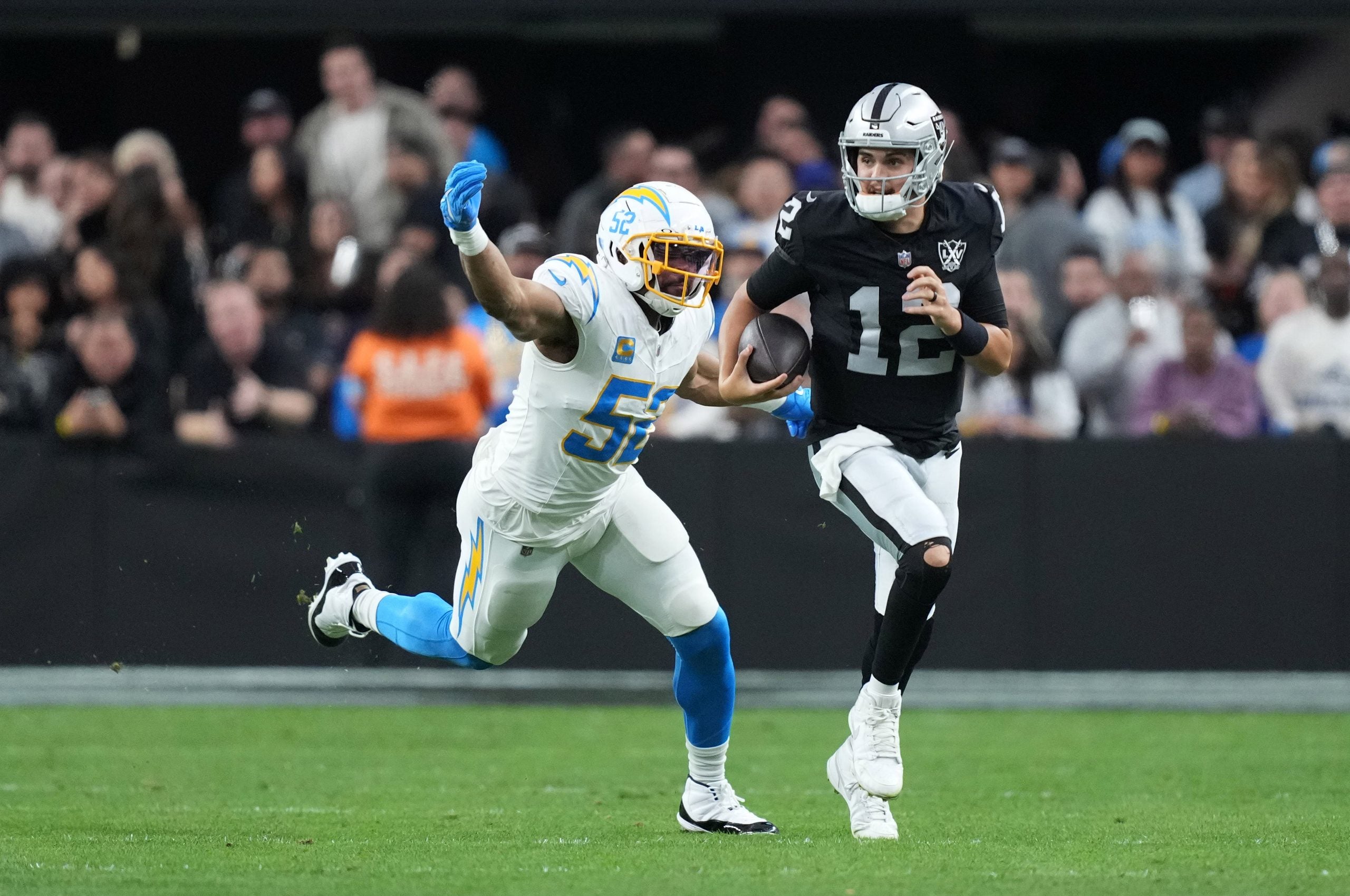 Jan 5, 2025; Paradise, Nevada, USA; Las Vegas Raiders quarterback Aidan O'Connell (12) carries the ball against Los Angeles Chargers linebacker Khalil Mack (52) in the second half at Allegiant Stadium.